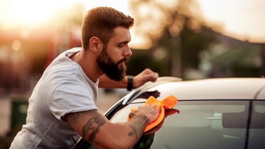 Man washing the rear window of a car.